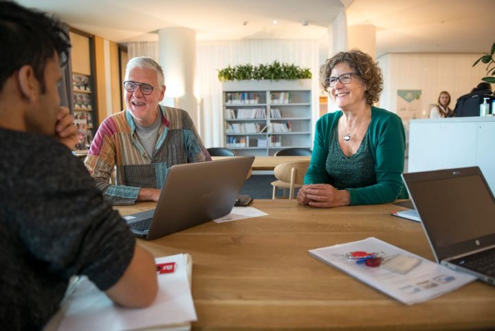 Drie personen aan tafel hebben een gesprek